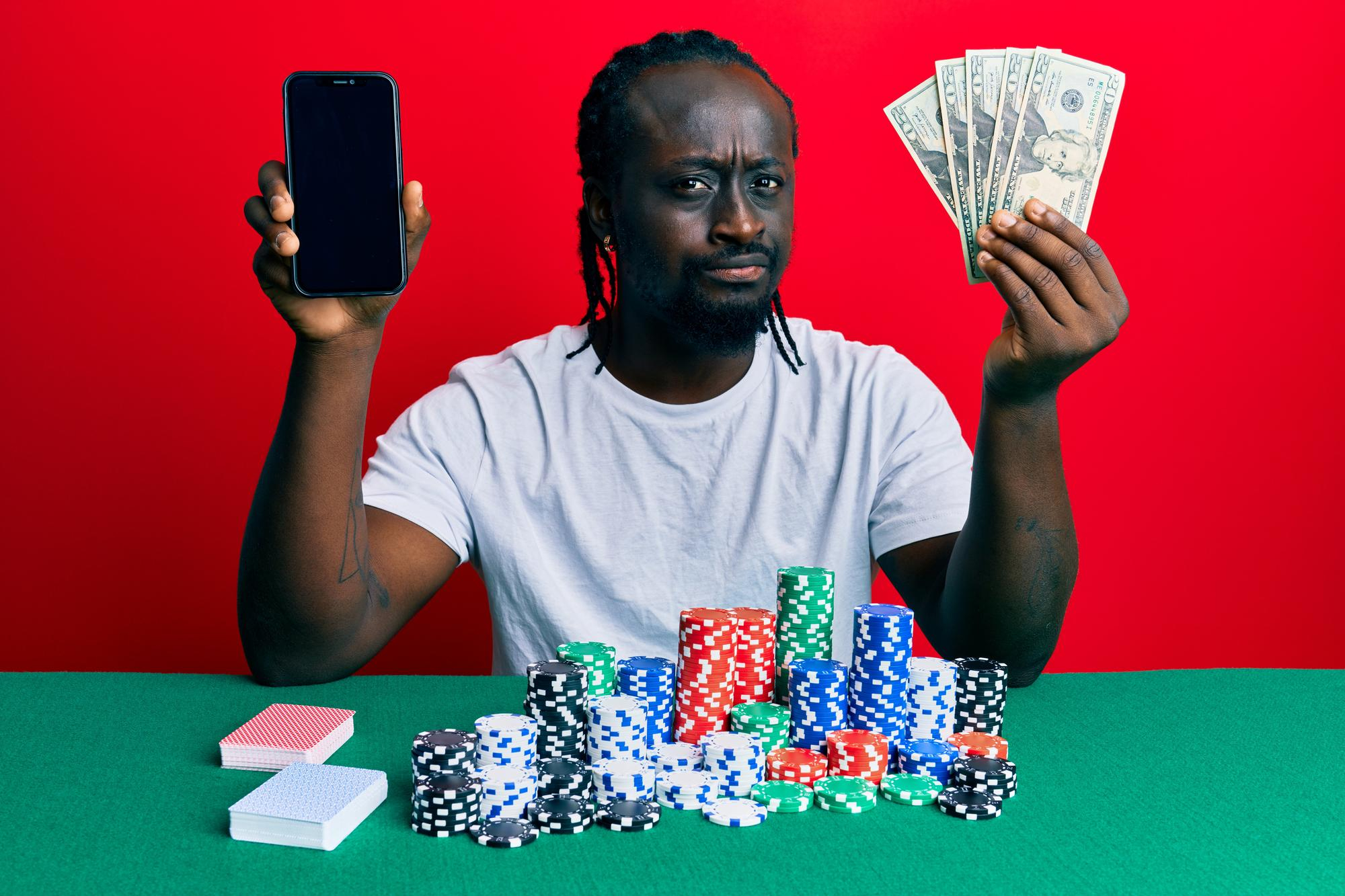 handsome-young-black-man-playing-poker-holding-smartphone-dollars-skeptic-nervous-frowning-upset-because-problem-negative-person
